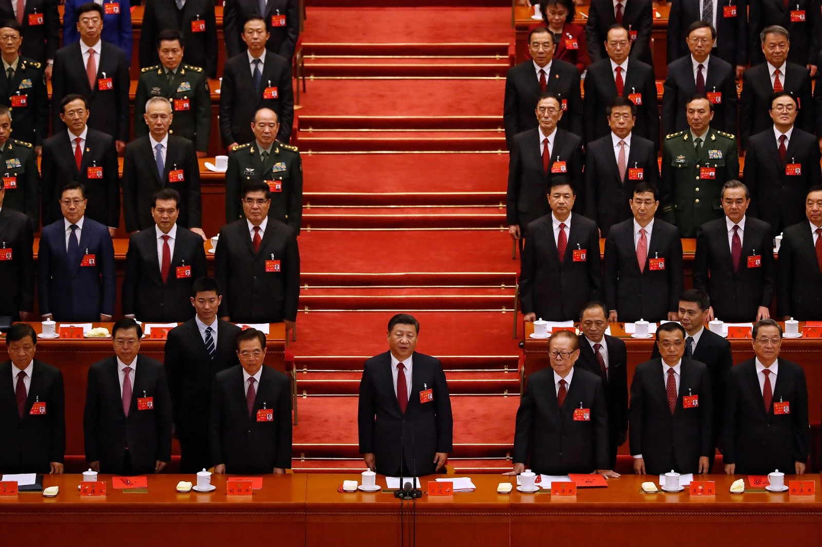 Chinese Communist Party members stand in a room with a red carpet.